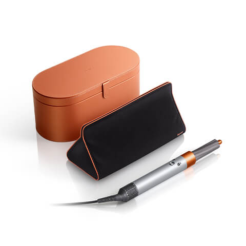 Copper presentation case in the background with triangular travel bag and a silver copper Dyson Airwrap™ styler Complete in the foreground