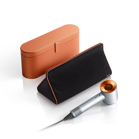 Copper presentation case in the background with triangular travel bag and a silver copper Dyson Supersonic hair dryer in the foreground